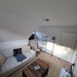 Wohnzimmer mit Sofa, Couchtisch und Kleiderständer unter schrägem Dach