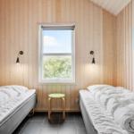 Two single beds, window with view of green, wooden walls and stool.