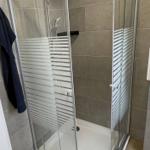 Shower cabin with glass door and showerhead. Floor and walls are tiled.