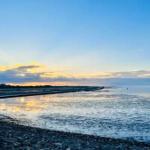 Sunset over water with sloping beach and reflections on the surface.
