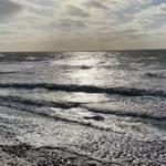 Waves break on a sandy beach under a cloudy sky.