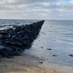 Rock breakwater extends into the sea. Sandy beach with calm waves.