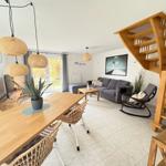 Living and dining area with wooden staircase, sofa, dining table, and pendant lights.