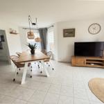 Living and dining area with wooden table, TV, and kitchen area in the background.