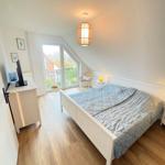 Bedroom with sloped ceiling, bed, TV stand, and balcony door.