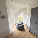 Room with gray bean bag, wooden floor, and large window with view.