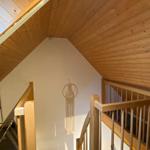 Wood-paneled ceiling and staircase with handrail. A macrame object hangs on the wall.