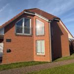 Two-story house with red tiled roof and balcony. Green lawns and paved paths.
