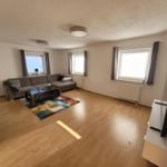 Living room with sofa, coffee table, and TV. Wooden floor and windows with curtains.