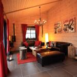 Wohnzimmer mit Holzwand, roten Vorhängen, Ledersofa und Holztisch.