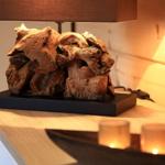 Tischlampe mit Holzskulptur auf Holzoberfläche, Kerzen im Hintergrund.