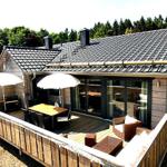 Terrasse mit Tisch, Stühlen und Sonnenschirmen vor einem Holzhaus mit Glasfront.