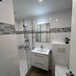 Badezimmer mit Dusche, Waschbecken und Toilette. Weiße Fliesen und Glaswand.