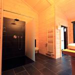 Badezimmer mit Dusche, Waschbecken und Heizung. Holzwände und dunkle Fliesen.