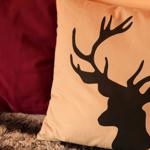 Kissen mit Hirschsilhouette neben einem roten Kissen auf einem Teppich.