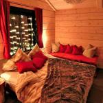 Schlafzimmer mit Holzwand, Bett, roten Kissen und Fenster mit Lichterkette.