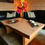 Ein Wohnzimmer mit schwarzen Sofas, einem rustikalen Holztisch und einer Blumenvase.