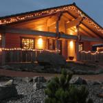 Holzhaus mit Lichterketten an Dach und Balkon, gepflasterte Umgebung mit Steinen und Pflanzen.