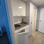 Küche mit Spüle, Kochfeld und Schränken. Tür führt in Schlafzimmer.