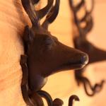 Metallfigur eines Hirschkopfes an einer Holzwand montiert, mit sichtbaren Haken darunter.
