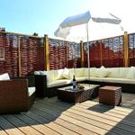 Terrasse mit Sitzgruppe, Sonnenschirm und Holzgeländer.