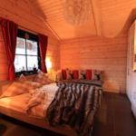 Schlafzimmer mit Holzwand, Bett, Fenster mit roten Vorhängen und Schrank.