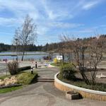 Pflasterweg führt zu einem See mit Bäumen und einem Mehrfamilienhaus.