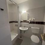 Badezimmer mit Dusche, Waschbecken und Toilette. Weiße Fliesen und runde Spiegel.