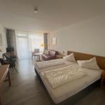 Zimmer mit Doppelbett, Sofa, Schreibtisch und TV. Blick auf Balkon durch Fenster.