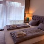 Doppelbett mit Bettwäsche, Nachttisch und Lampe neben großem Fenster mit Jalousie.