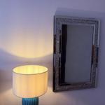 Lampe neben Spiegel an Wand. Spiegel hat glitzernden Rahmen.