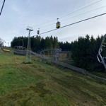 Ski lift mit Gondeln und Schienen auf grünem Hang vor Wald