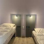 Zwei Einzelbetten mit weißen Bettwäschen stehen in einem Raum mit lila Wänden und Holzboden.