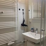 Badezimmer mit Dusche, Waschbecken und Heizkörper. Föhn hängt an der Wand.