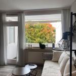 Wohnzimmer mit Sofa, zwei runden Tischen und Blick auf Bäume mit Herbstfarben.