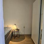 Schlafzimmer mit Bett, Nachttisch und Lampe. Holzboden und Schrank sichtbar.