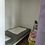 Schlafzimmer mit Bett, Nachttisch und Lampe. Holzfußboden und weiße Wände.