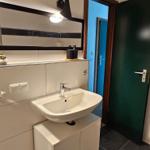 Bad mit Waschbecken, Spiegel und dunklem Bodenfliesen.