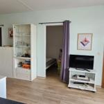 Wohnung mit Küche, Wohnbereich, Fernseher und Schlafzimmer. Holzboden und weiße Möbel.