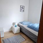 Schlafzimmer mit Bett, Nachttisch und Teppich auf Holzdielenboden.