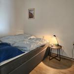 Schlafzimmer mit Bett, Nachttisch und Lampe. Holzdielenboden und Wandbild.