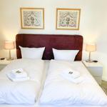 Doppelbett mit weißer Bettwäsche, zwei Nachttische mit Lampen und Bildern an der Wand.