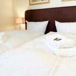 Zwei Betten mit weißen Bettwäsche und Handtüchern. Dunkelbrauner Kopfteil und Nachttischlampe.