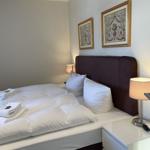 Doppelbett mit weißen Laken, zwei Nachttische und zwei Lampen an der Wand.