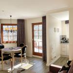 Wohn- und Essbereich mit Tisch, Stühlen und Fensterblick. Küche im Hintergrund.