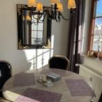 Runder Tisch mit Stühlen, Spiegel und Kronleuchter. Fenster mit Vorhängen.