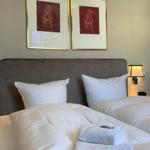 Ein Bett mit weißen Laken und zwei Kissen. Über dem Bett hängen zwei Bilder in goldenen Rahmen.