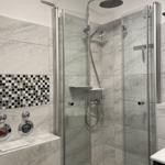 Duschkabine mit Glaswand, Duschbrause und Marmorfliesen.