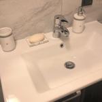 Waschbecken mit Wasserhahn, Seife und Flaschenhalter auf Marmorwand.