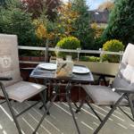 Terrasse mit Tisch und zwei Stühlen, umgeben von Bäumen und Sträuchern.